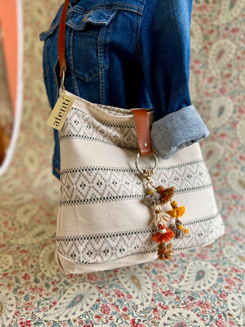 Atenti Dune Soft Tote with narrow dark geometric bands on cream fabric, brown strap and a multicolor tassel charm.