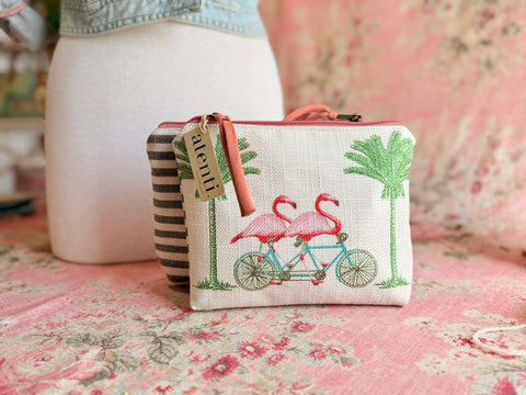 Small pouch with flamingo design on a floral surface. Small zipper pouch with flamingo bicycle print, palm trees, and black striped gusset