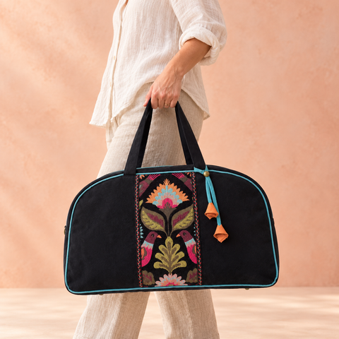 Lovebirds black velvet patchwork Overnighter carried by hand, showing colorful bird tapestry and turquoise trim