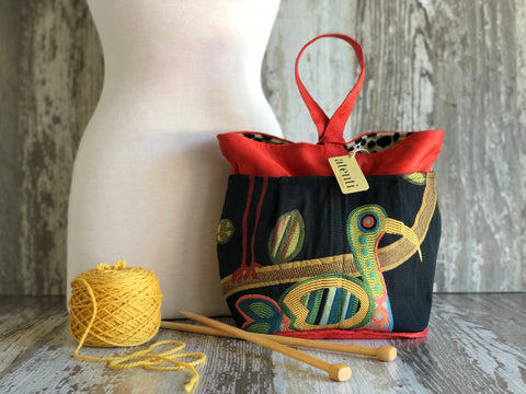 A tall caddy with a black base and red accents, featuring a colorful bird pattern. It has a handle and stands upright.